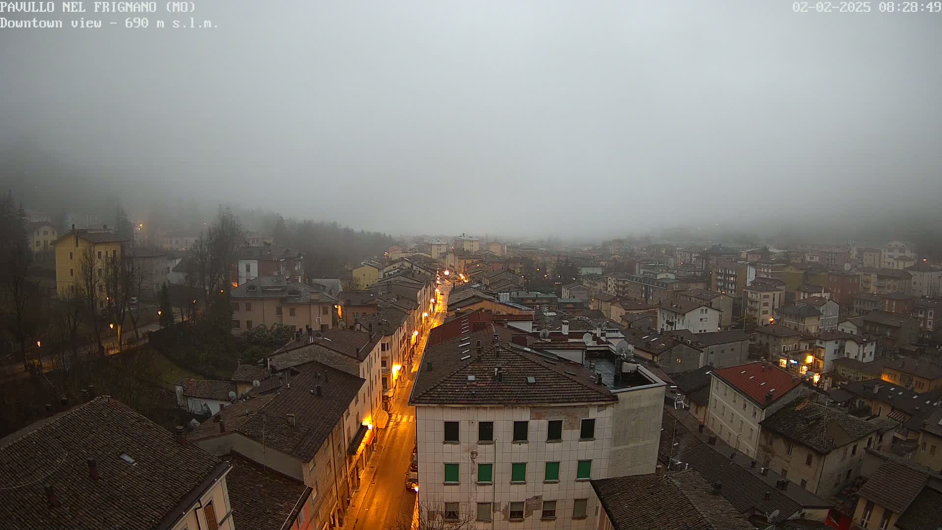 A foggy town is seen from above, with a long, illuminated street running through its center.