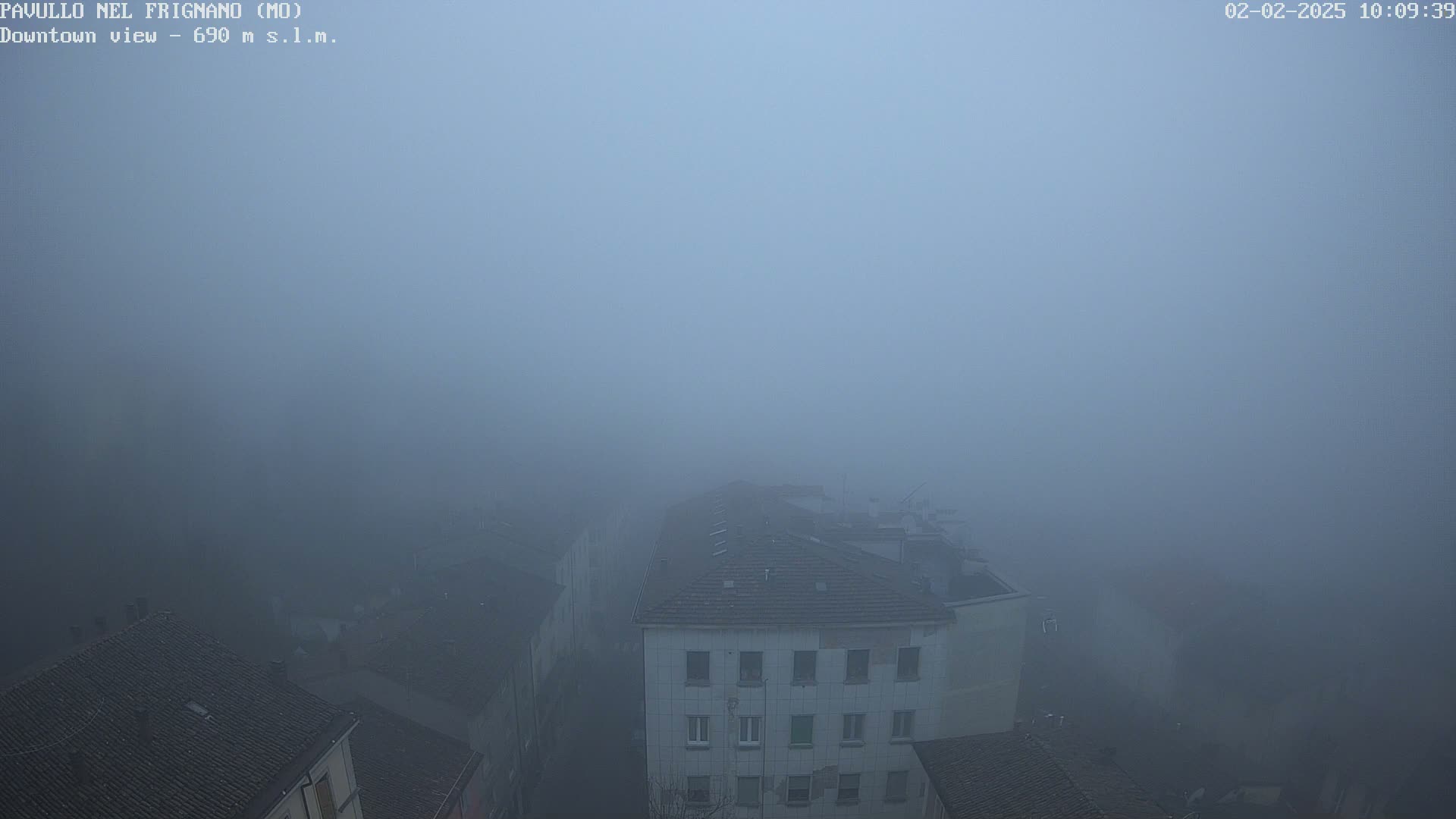 A thick fog obscures a view of several buildings' rooftops and upper stories.