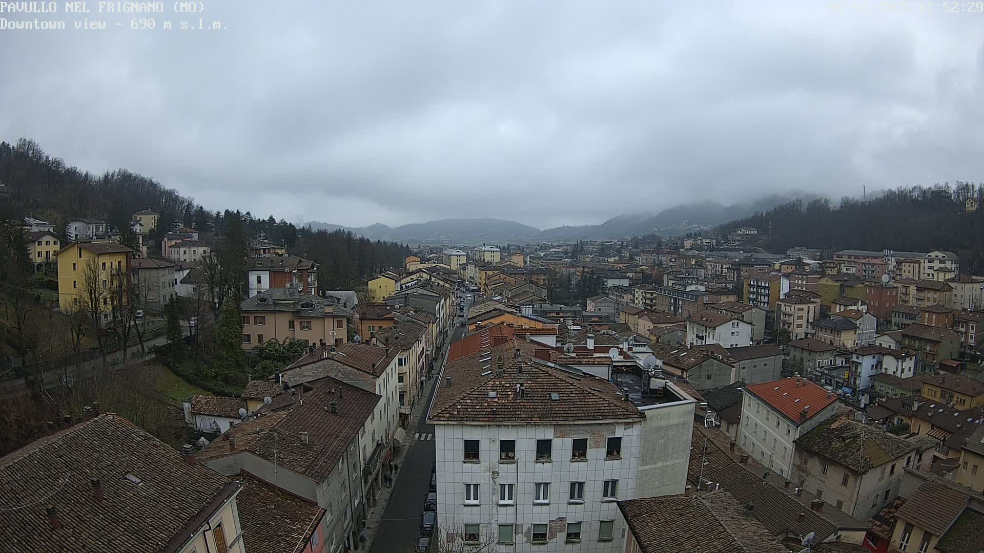 An overcast day reveals a sprawling town nestled in a valley surrounded by tree-covered hills.