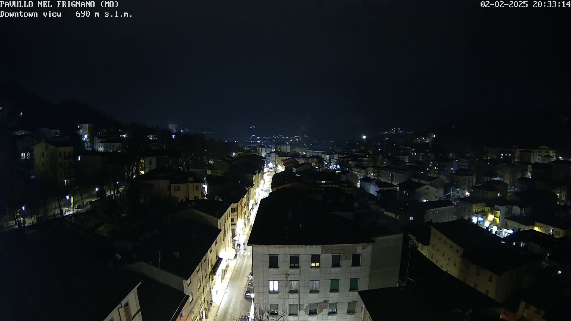 A nighttime, high-angle view of a town with a main street illuminated, nestled in a valley under a dark sky.