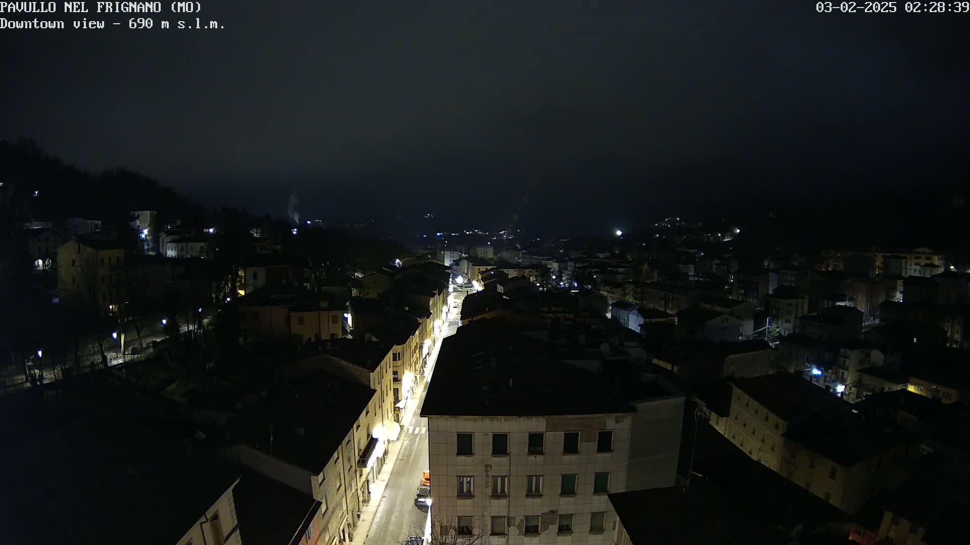 A nighttime, high-angle view of a town with a long, brightly lit street cutting through the dark buildings and hills.