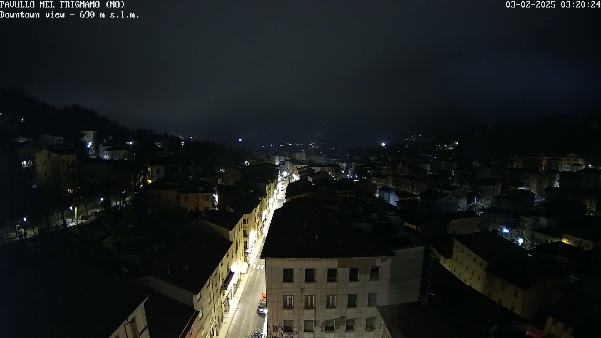 A nighttime, high-angle view of a town with dimly lit buildings and streets under a dark, possibly overcast sky.