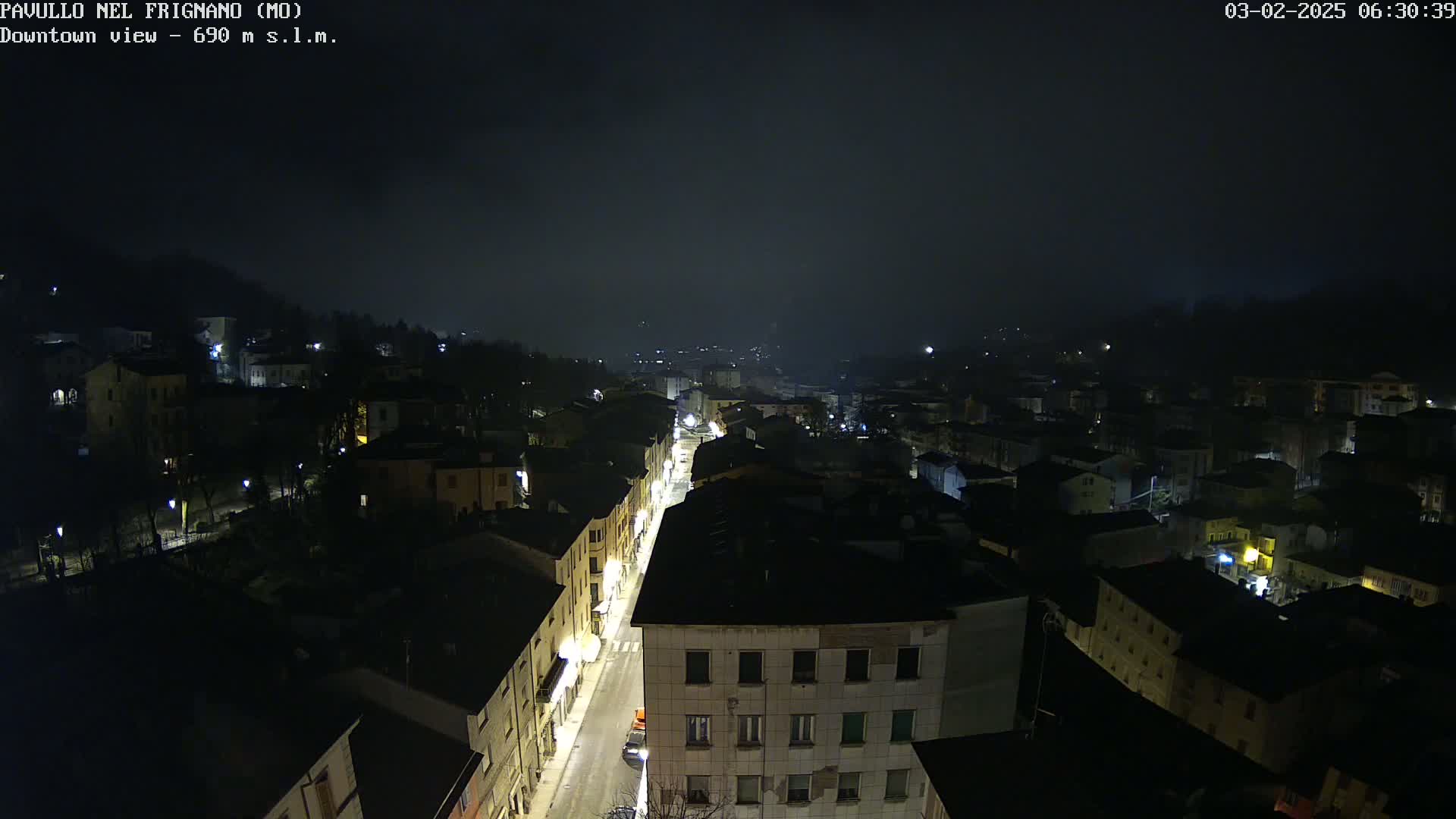A nighttime aerial view of a town shrouded in fog, with dimly lit buildings and streets.