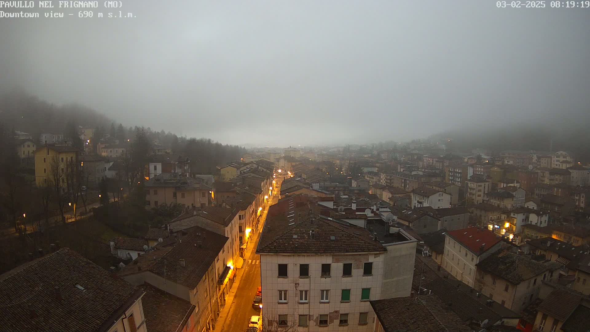 A foggy, dimly lit town is viewed from above, showing a long street lined with buildings.