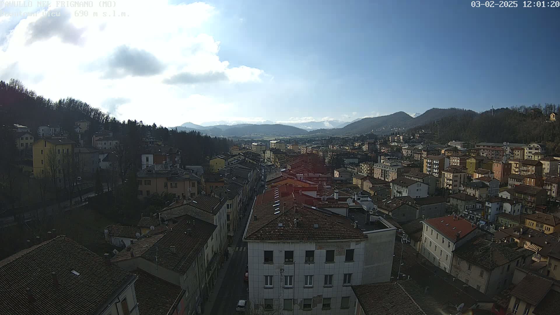 A partly sunny day reveals a sprawling town nestled in a valley, surrounded by hills and mountains.