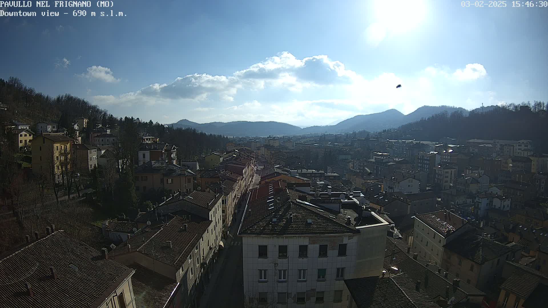 A sunny day reveals a sprawling town nestled in a valley, surrounded by hills and mountains under a partly cloudy sky.