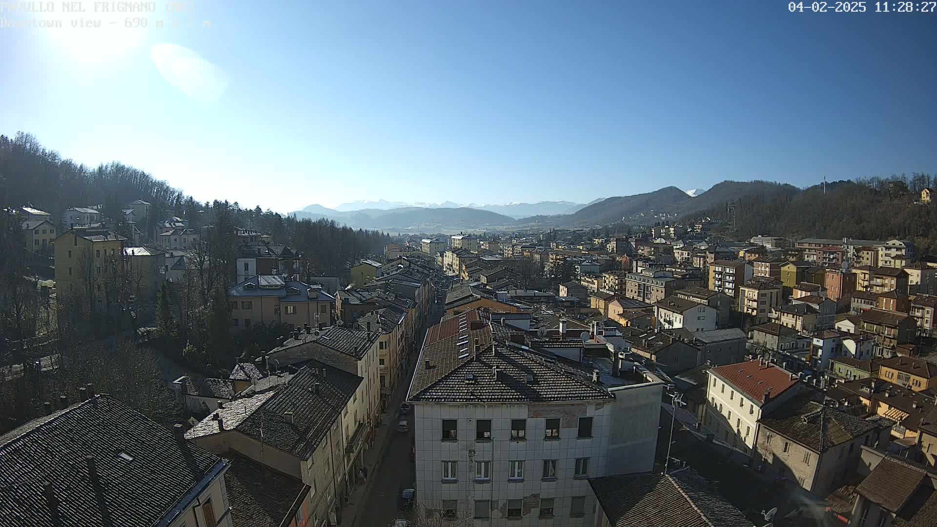 A sunny day reveals a sprawling town nestled in a valley, surrounded by mountains and trees.