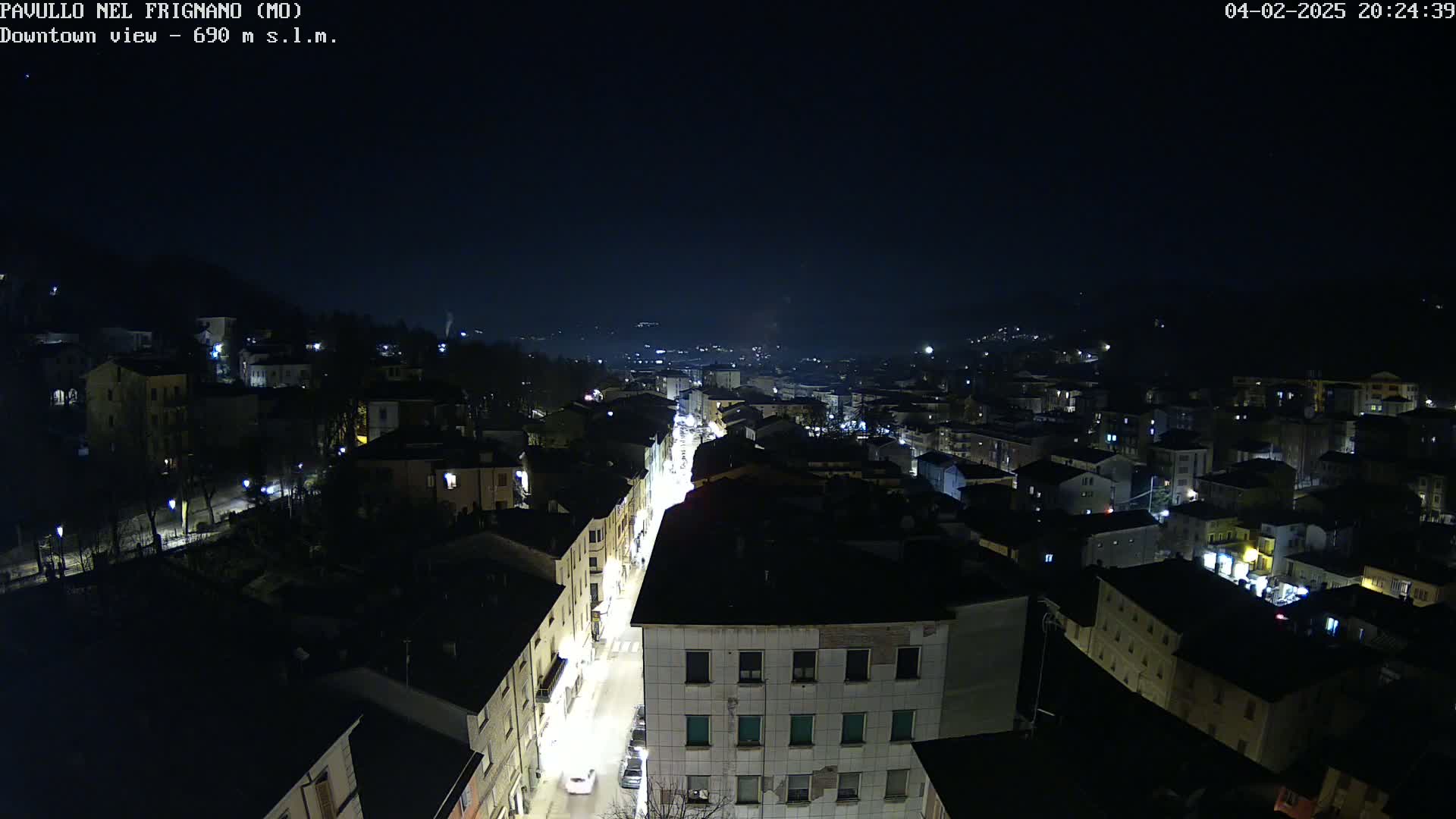 A nighttime, high-angle view of a town, showing a street lined with buildings and illuminated by lights.