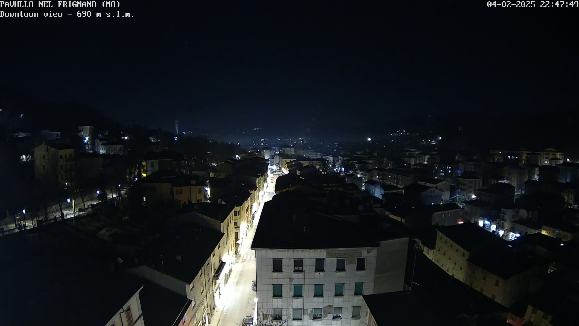 A nighttime, high-angle view shows a town with illuminated streets and buildings under a clear, dark sky.