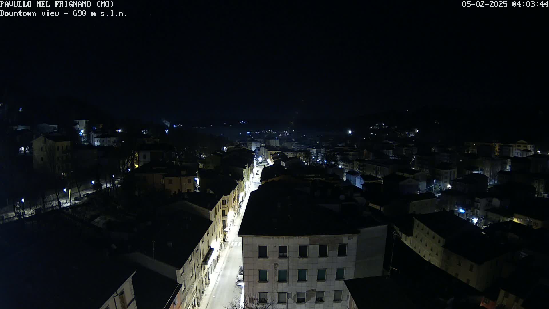 A nighttime, high-angle view shows a town's streetlights illuminating buildings and a road.