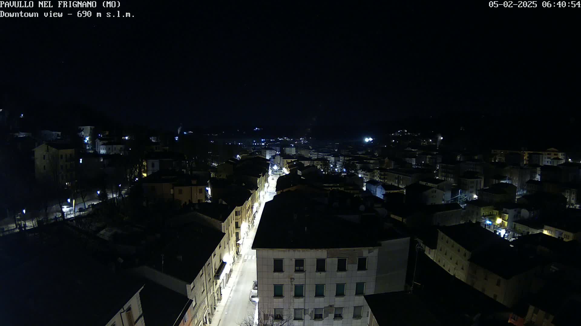 A nighttime, high-angle view of a town's street and buildings illuminated by streetlights under a clear, dark sky.