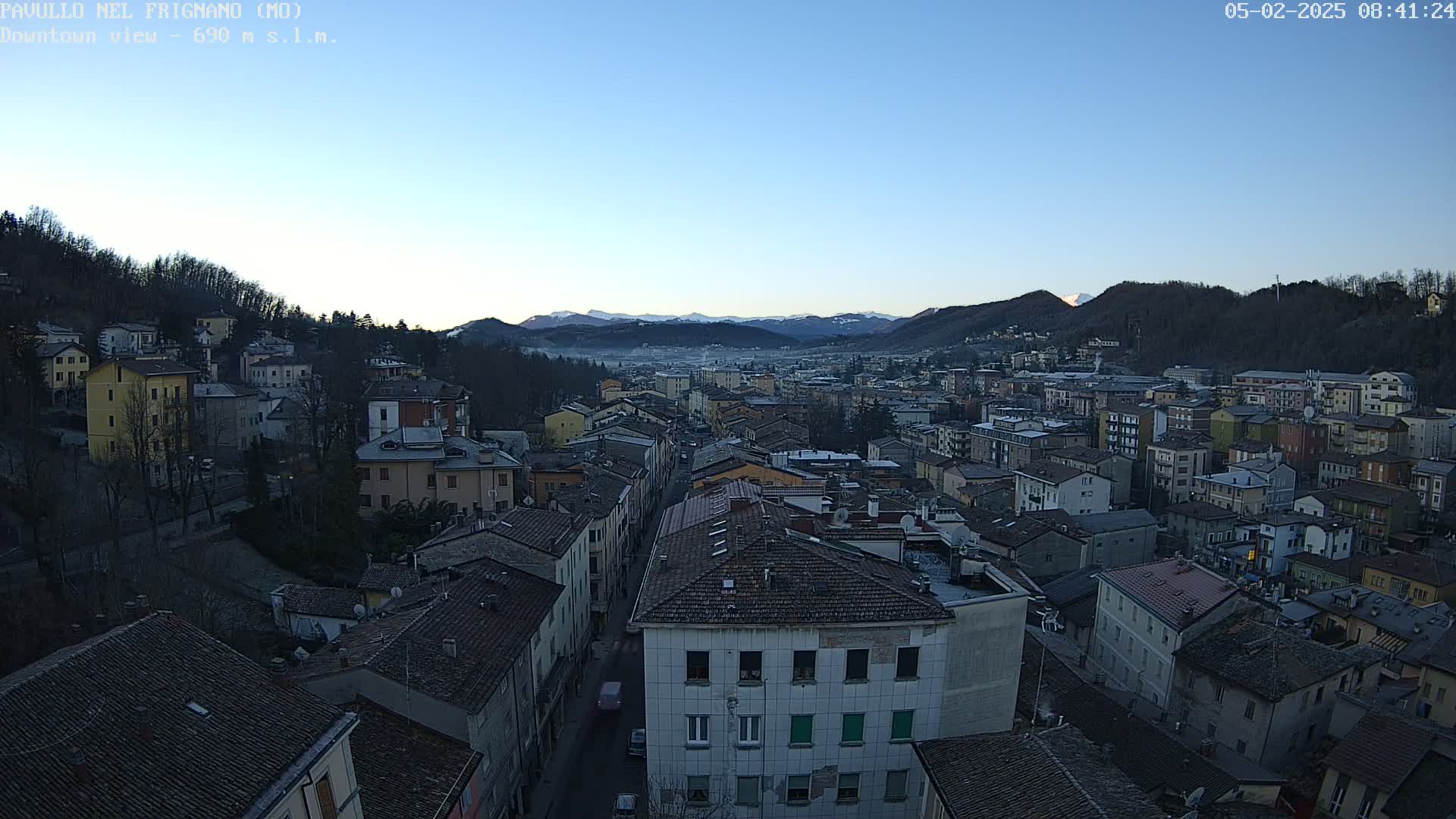 A clear, twilight view of a town nestled in a valley, surrounded by mountains.