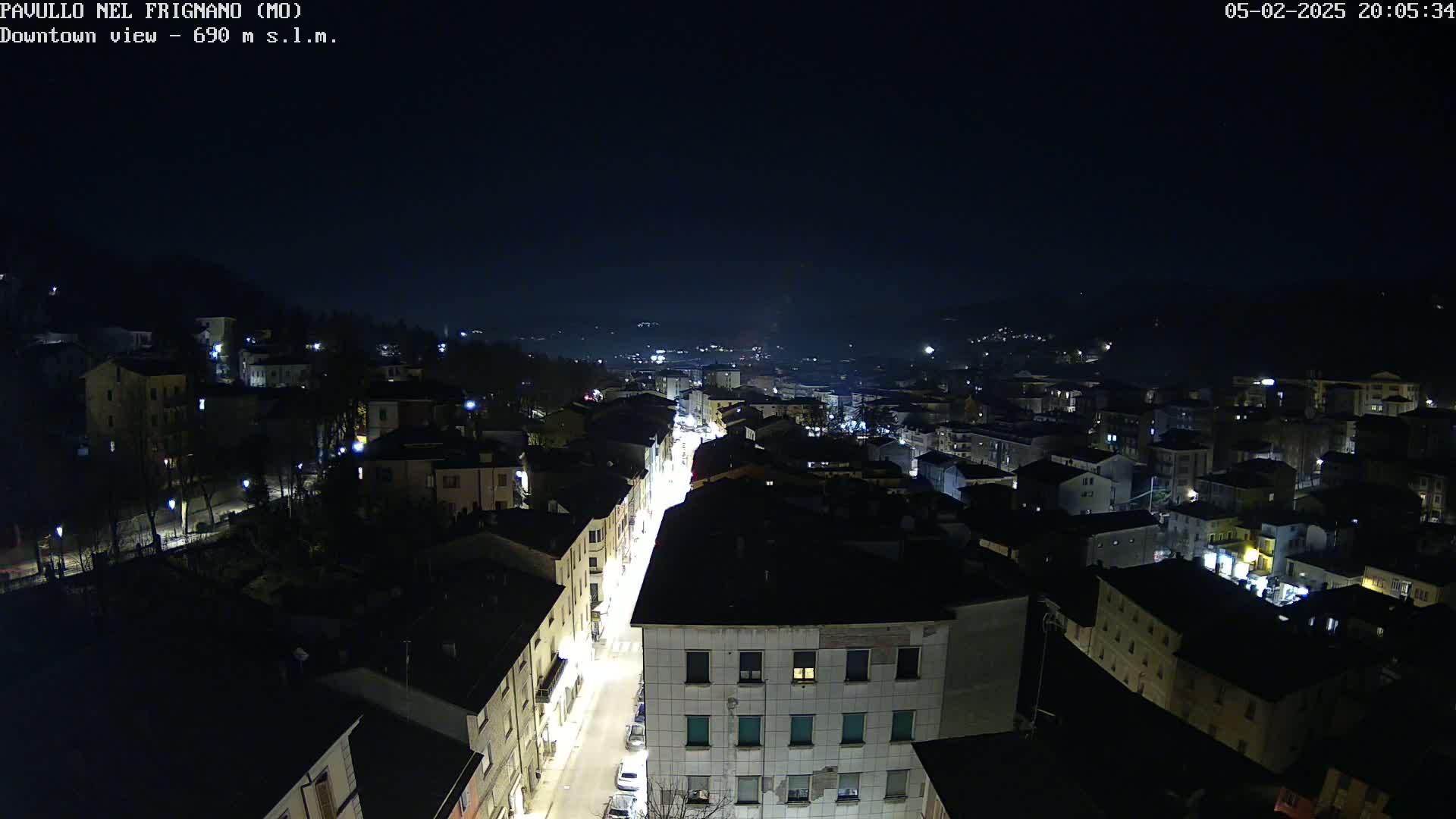 A nighttime aerial view shows a town with illuminated streets and buildings under a clear, dark sky.