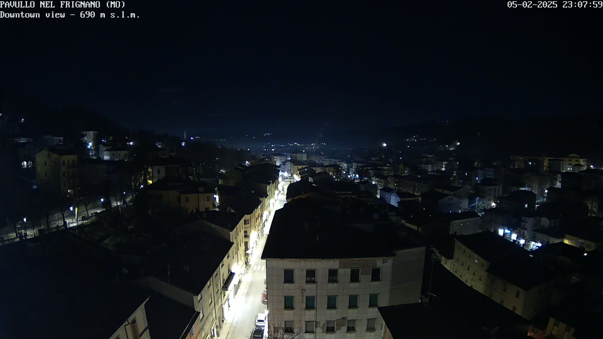 A nighttime aerial view of a town shows a street lined with buildings, lit by streetlights under a clear, dark sky.