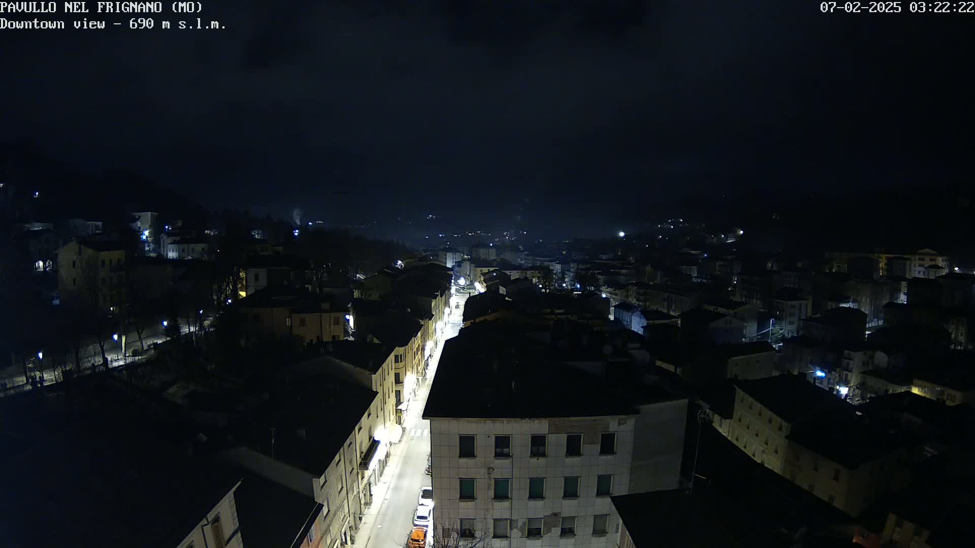 A nighttime, high-angle view of a town with dimly lit buildings and a street running through the center.