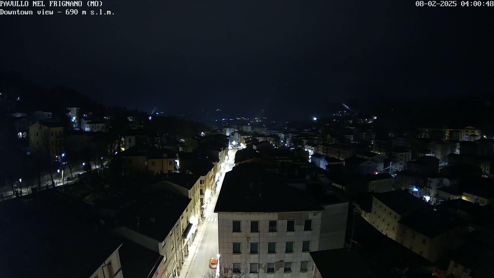 A nighttime, high-angle view of a town with dimly lit streets and buildings, under a dark, cloudy sky.