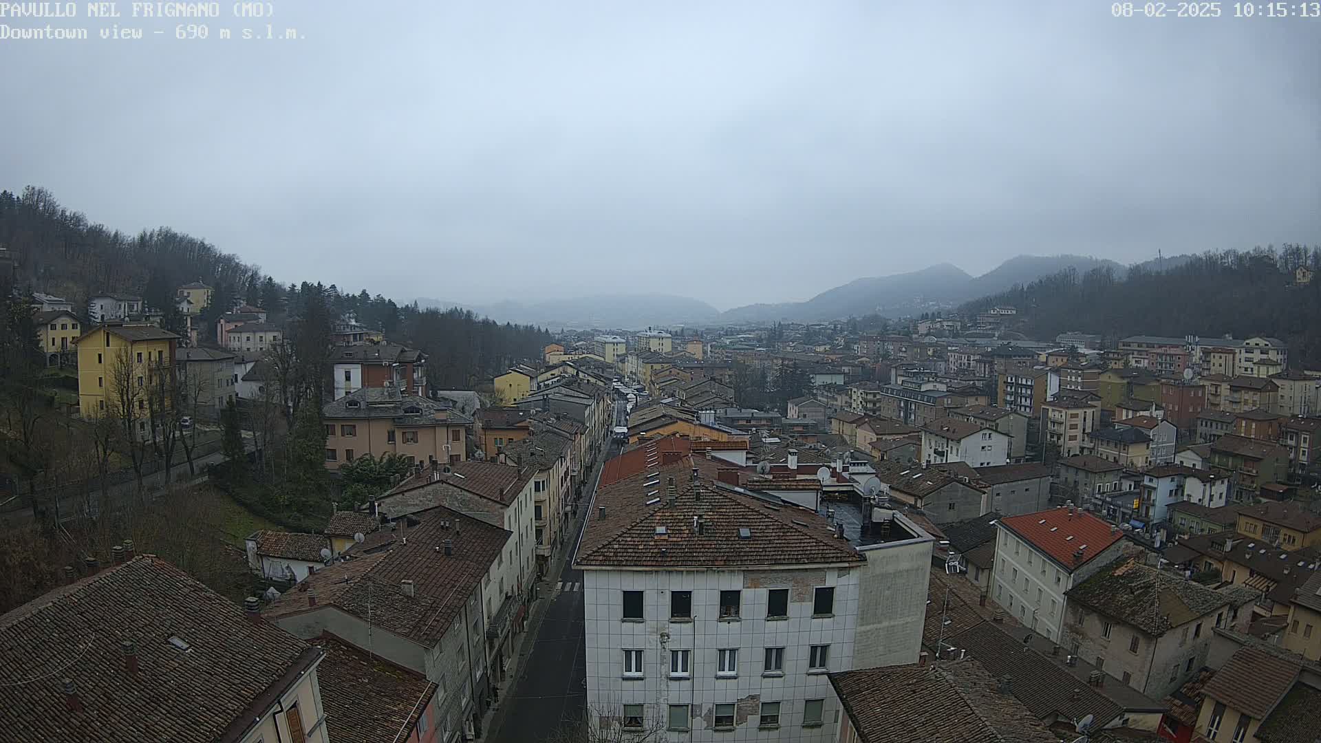 A sprawling town nestled in a valley under a cloudy sky, with buildings of varying heights and colors extending into the distance.