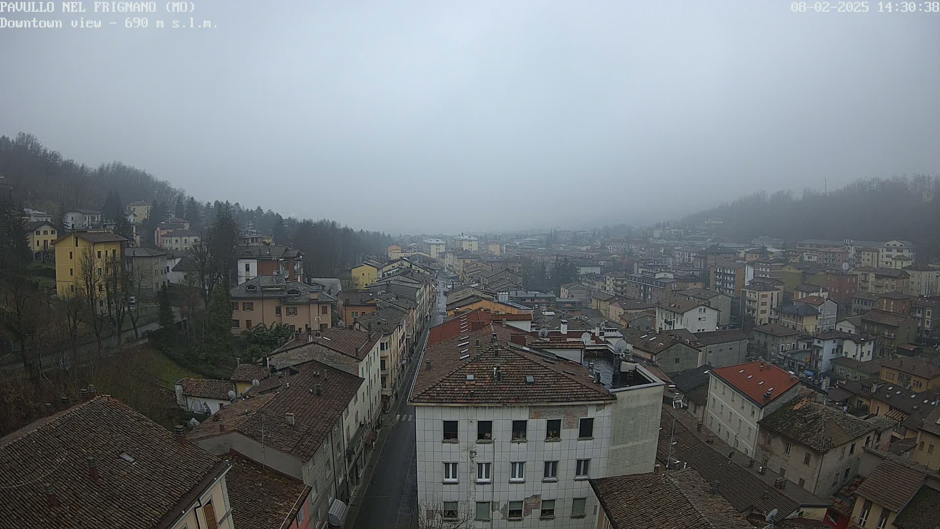A foggy view of a town, seen from above, shows many closely packed buildings with brown roofs.