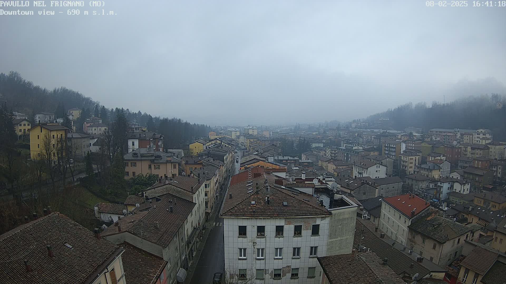A foggy view of a town's rooftops and streets, nestled between hillsides.