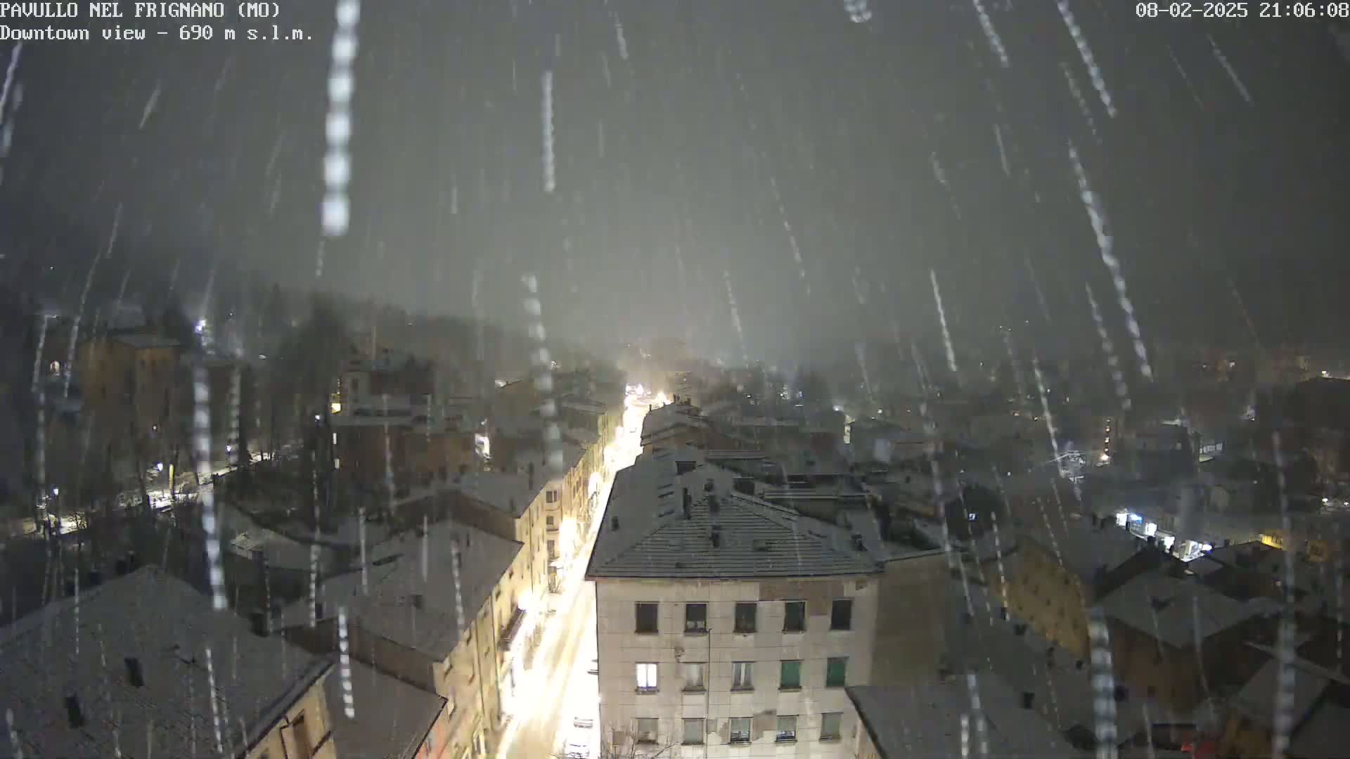 A snow-covered town is viewed from above at night, with snow falling heavily.