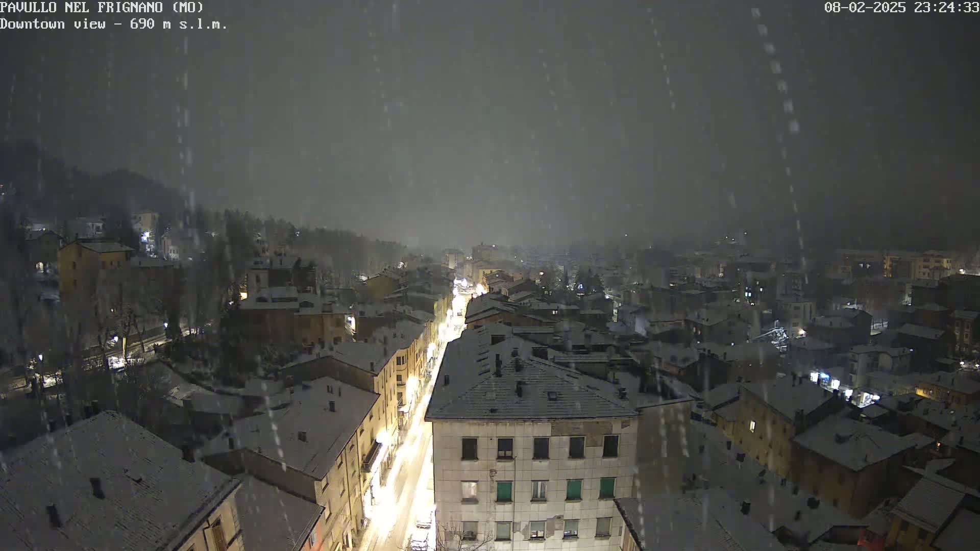 A nighttime view of a snow-covered town, illuminated by streetlights, with snow falling.