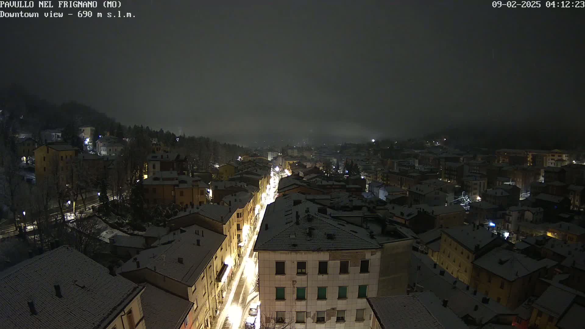 A nighttime aerial view of a snow-covered town under a foggy sky.