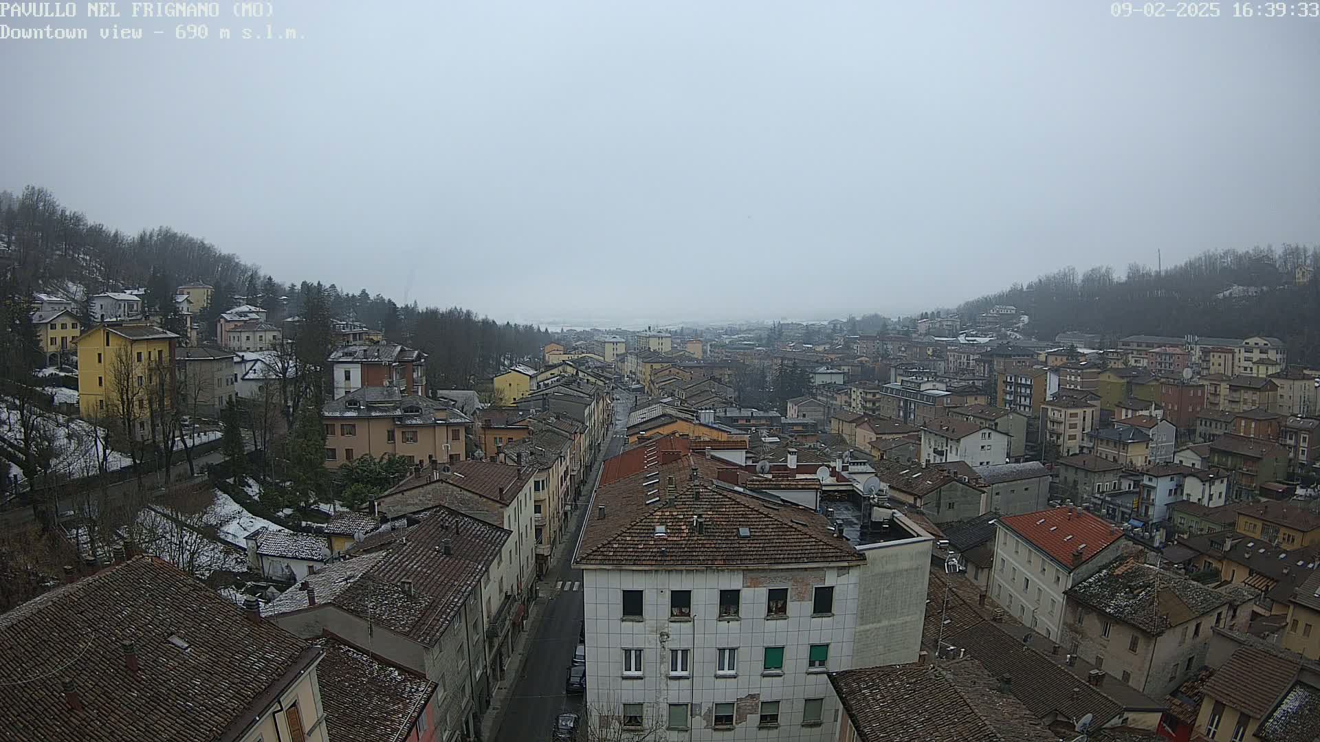 A wide shot shows a town covered in light snow under an overcast sky, with a long street running through the center of the image.