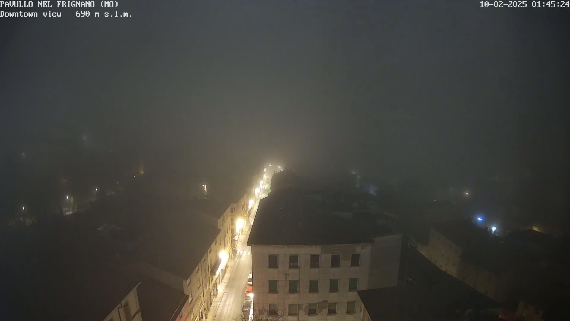 A foggy night scene shows a street lined with buildings, dimly lit by streetlights.