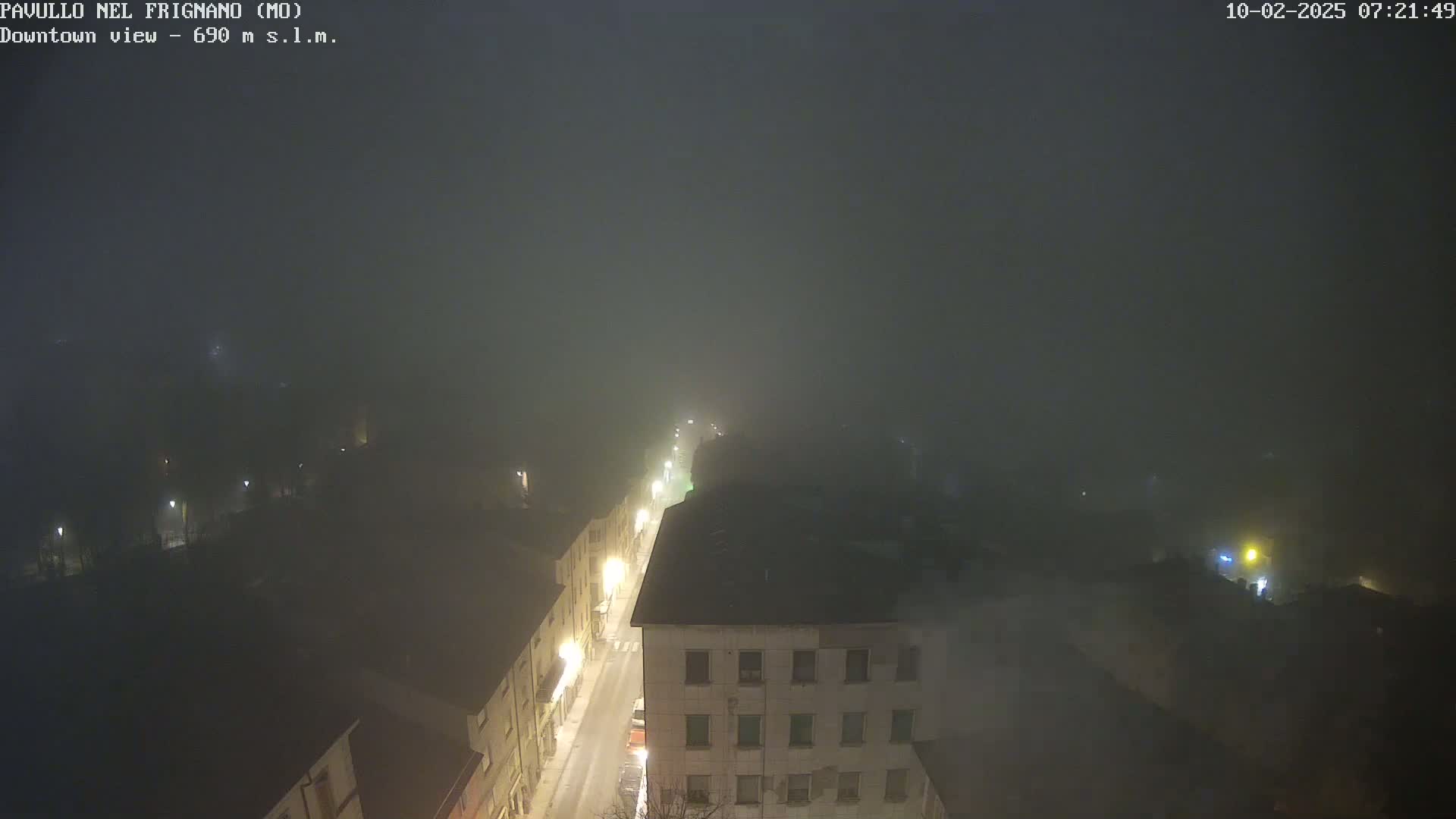 A nighttime, foggy view of a town's street, showing buildings and dimly lit streets.
