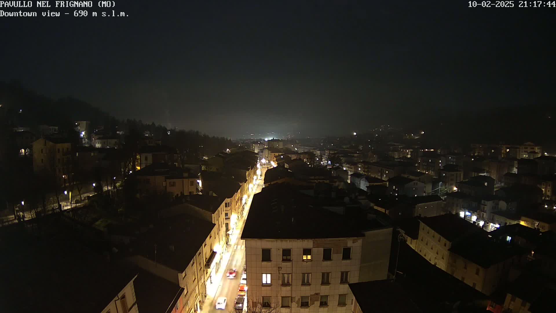 A nighttime, hazy view of a town's downtown area with streetlights illuminating buildings and vehicles on a street below.