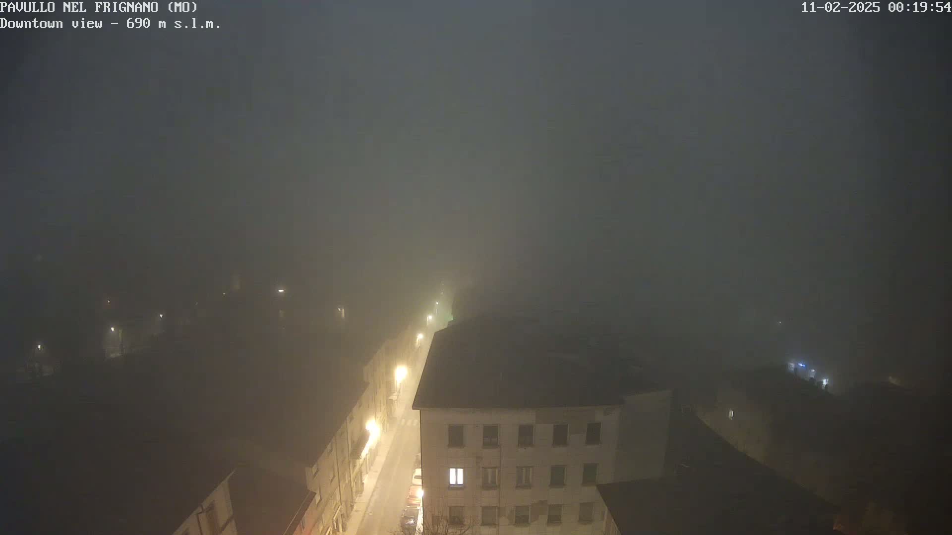 A nighttime, foggy view of a town, showing dimly lit buildings and streets.