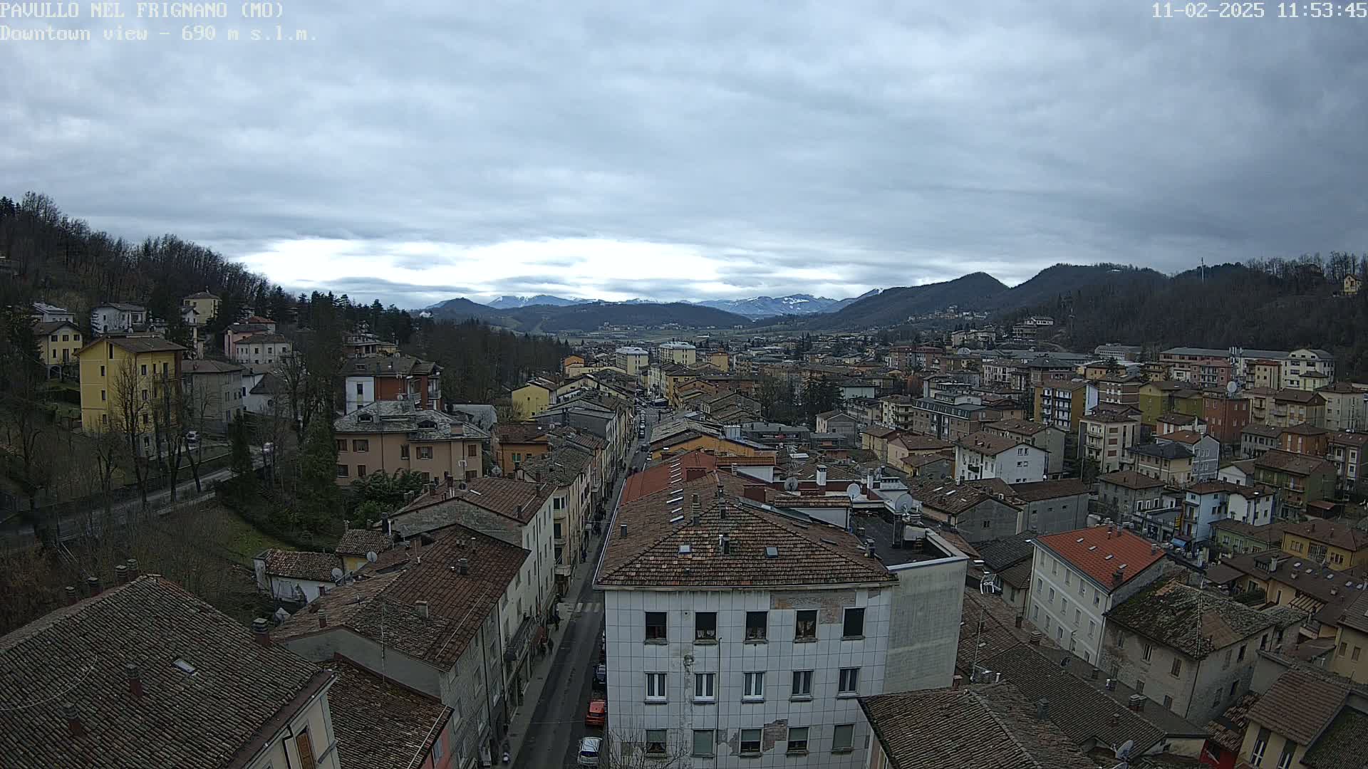 A sprawling town nestled in a valley under a cloudy sky, with distant snow-capped mountains visible in the background.