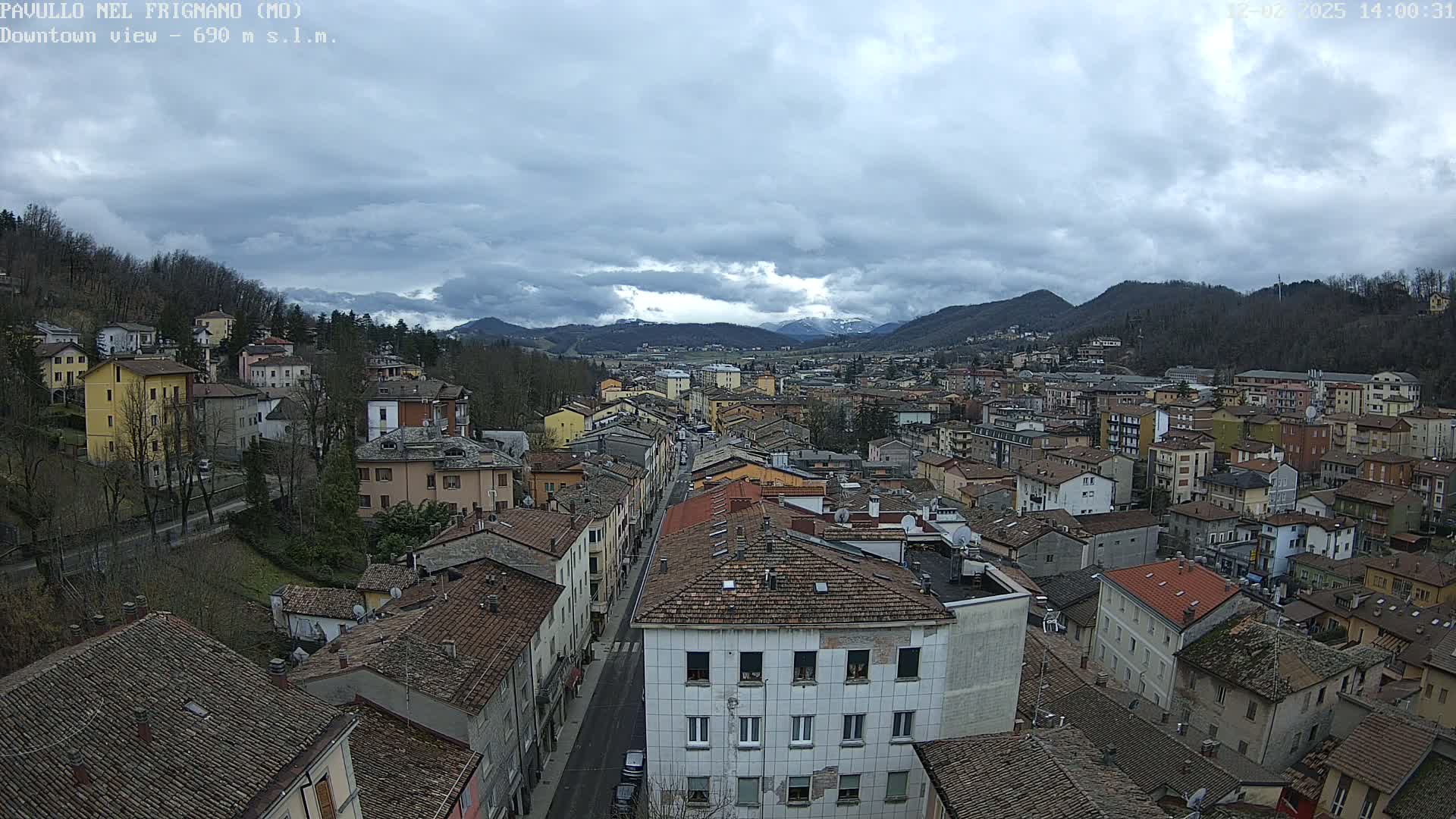 A town nestled in a valley under a cloudy sky, with mountains visible in the distance.