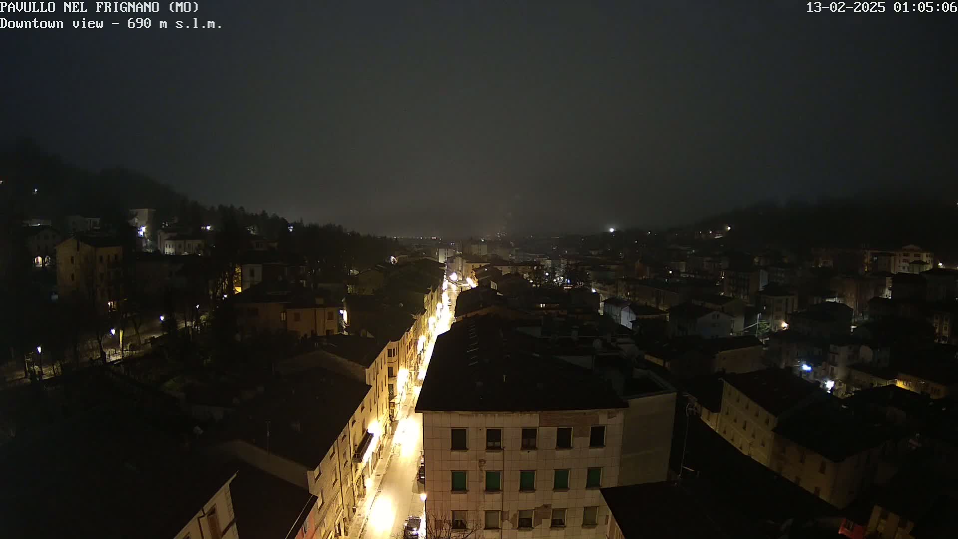 A nighttime, foggy view of a town's illuminated streets and buildings, seen from an elevated perspective.