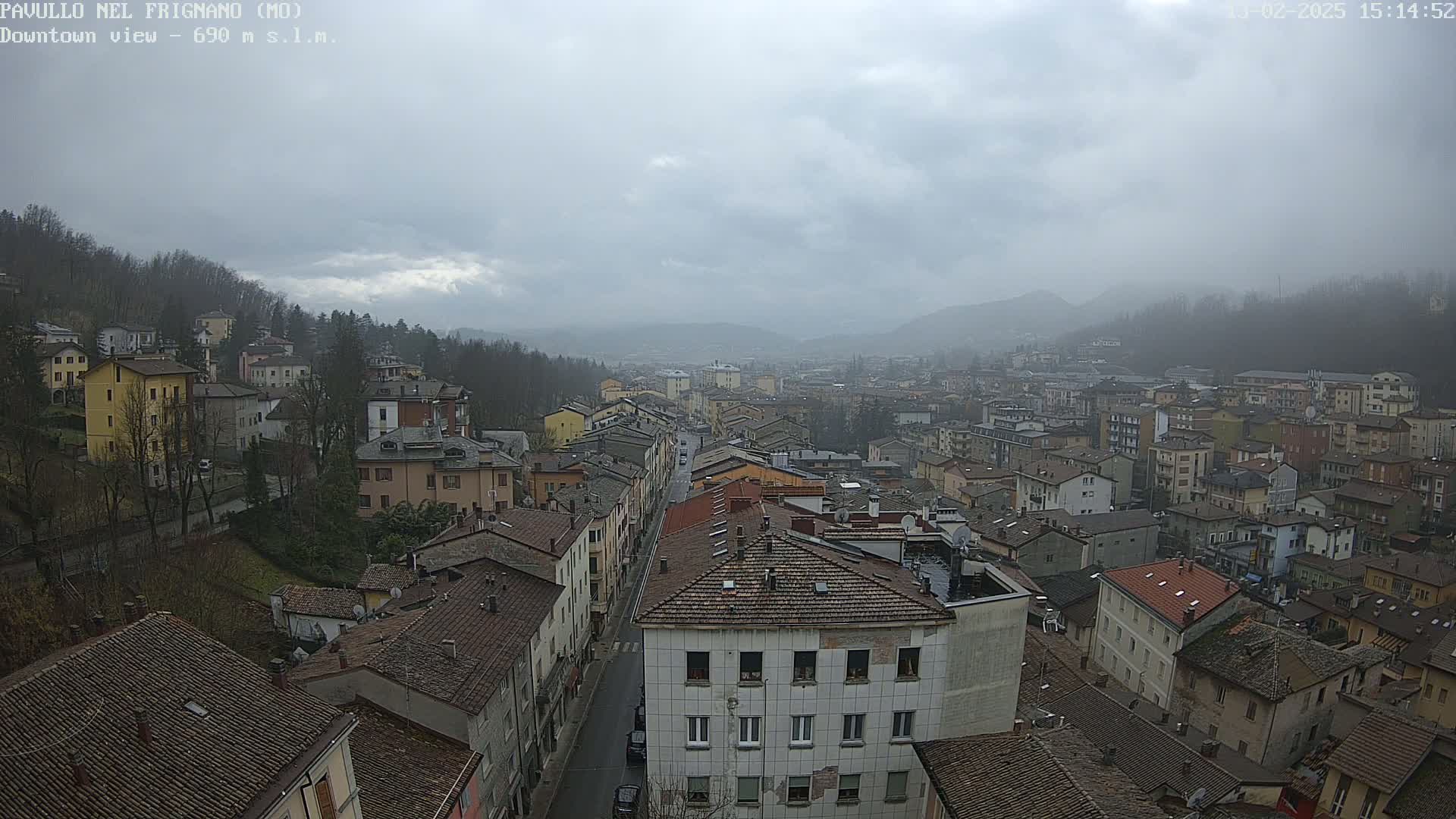 A wide view of a town nestled in a valley under an overcast sky, showing many buildings with dark-colored roofs.