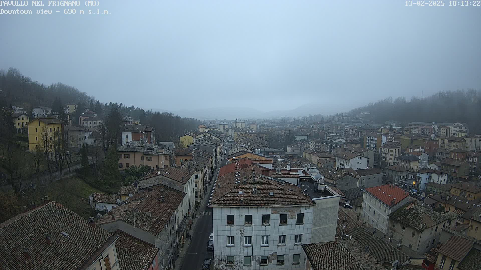 A hazy, overcast view of a town nestled in a valley, with numerous buildings and tree-lined hills visible in the distance.