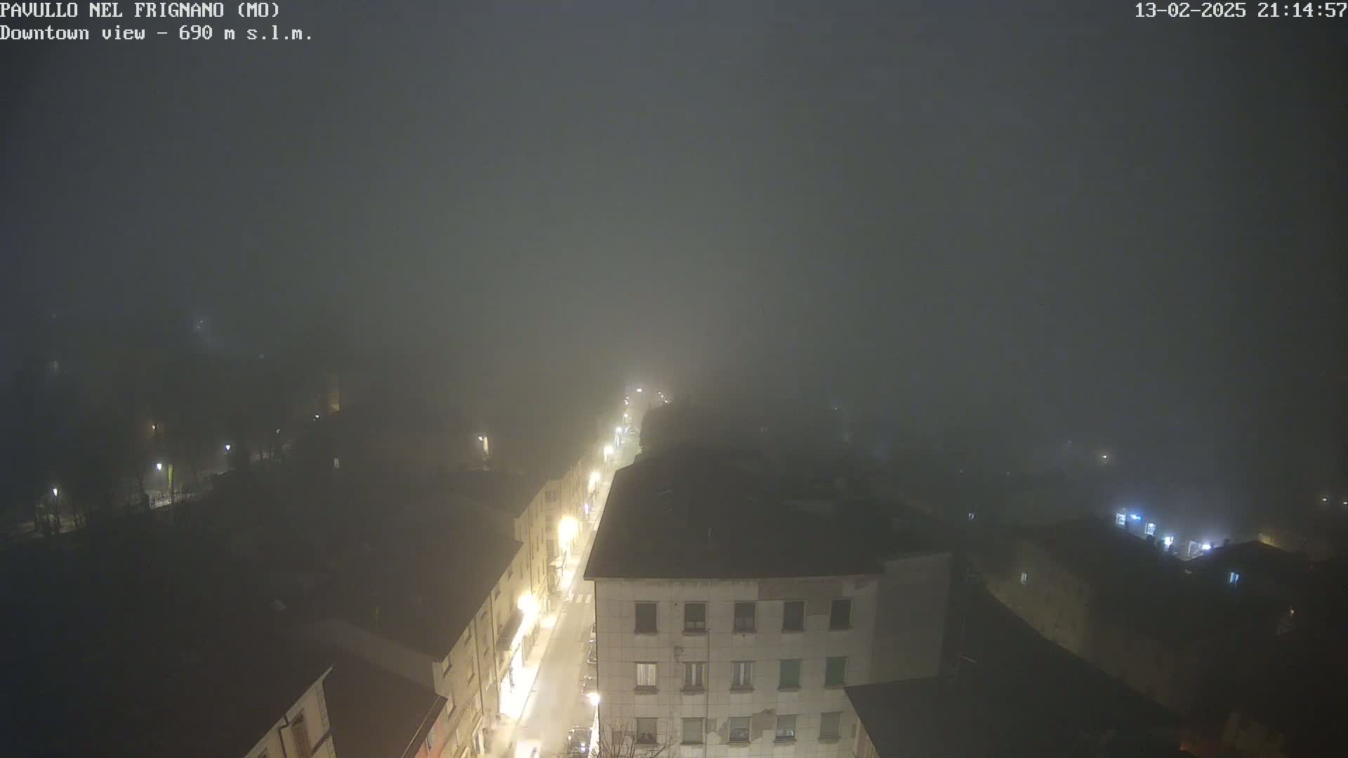 A nighttime, foggy view of a town's street and buildings, illuminated by streetlights.