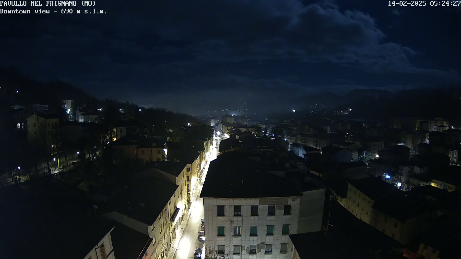 A nighttime, high-angle view of a town illuminated by streetlights under a dark, cloudy sky.