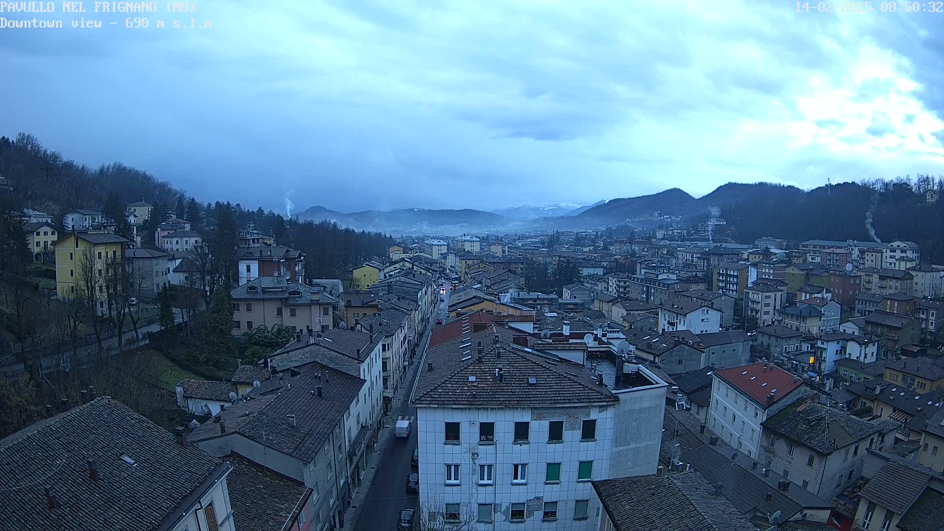 An overcast, dusky view of a town nestled in a valley between mountains.