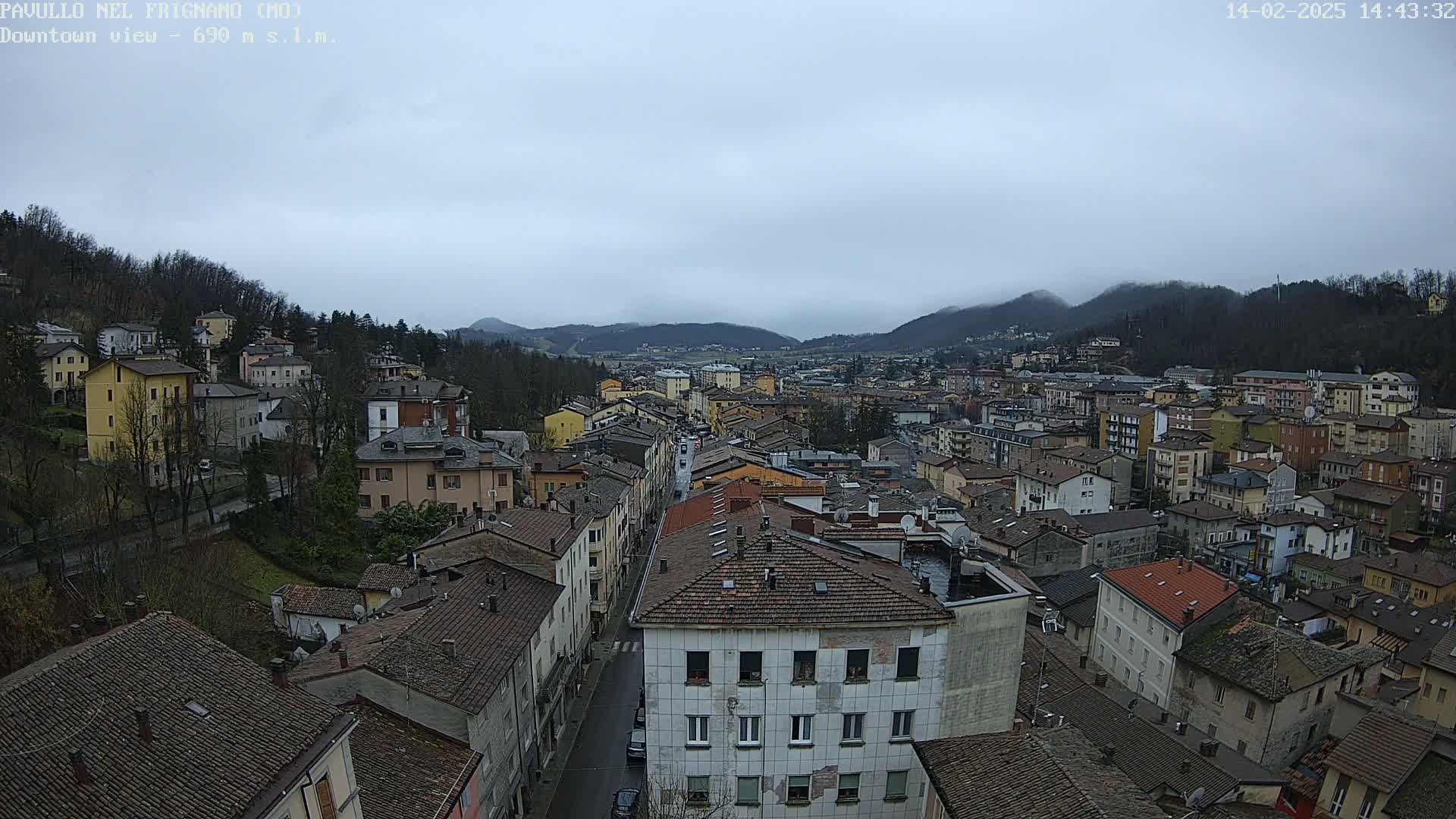 A sprawling town nestled in a valley between tree-covered hills under a cloudy sky.