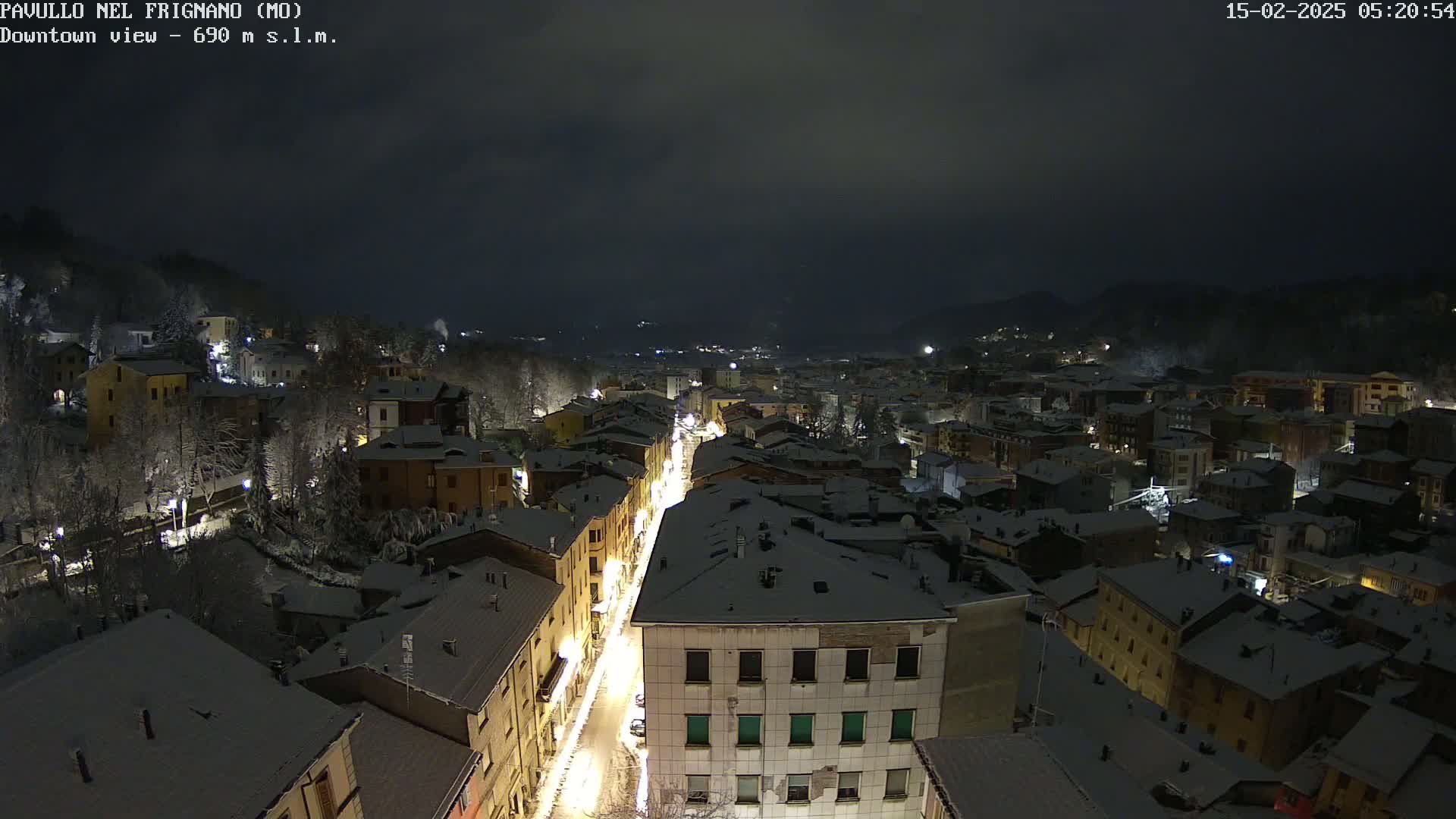 A snow-covered town at night, illuminated by streetlights, is viewed from above.