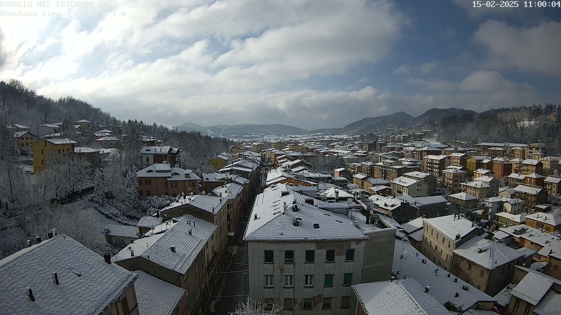 A snow-covered town nestled in a valley between hills, under a partly cloudy sky.
