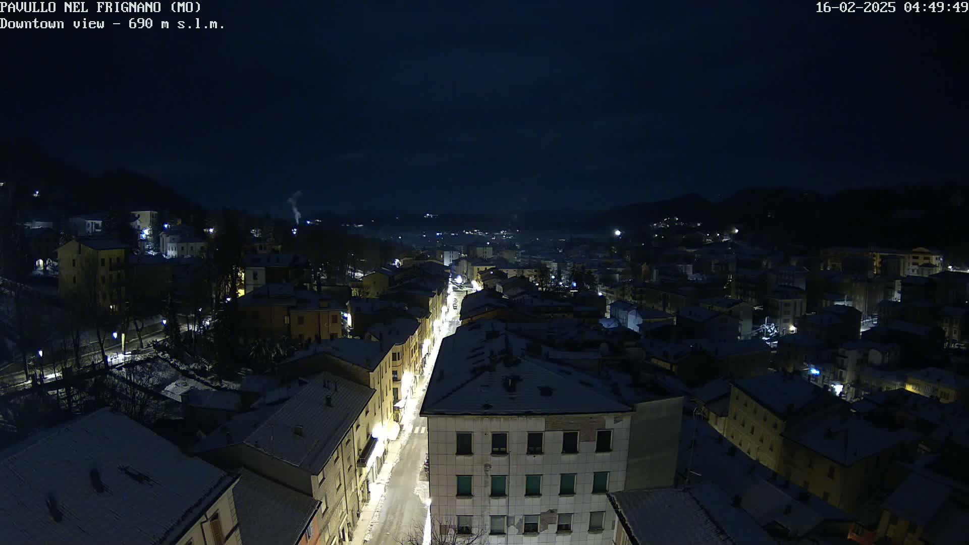 A snow-covered town at night is illuminated by streetlights, nestled in a valley under a dark sky.
