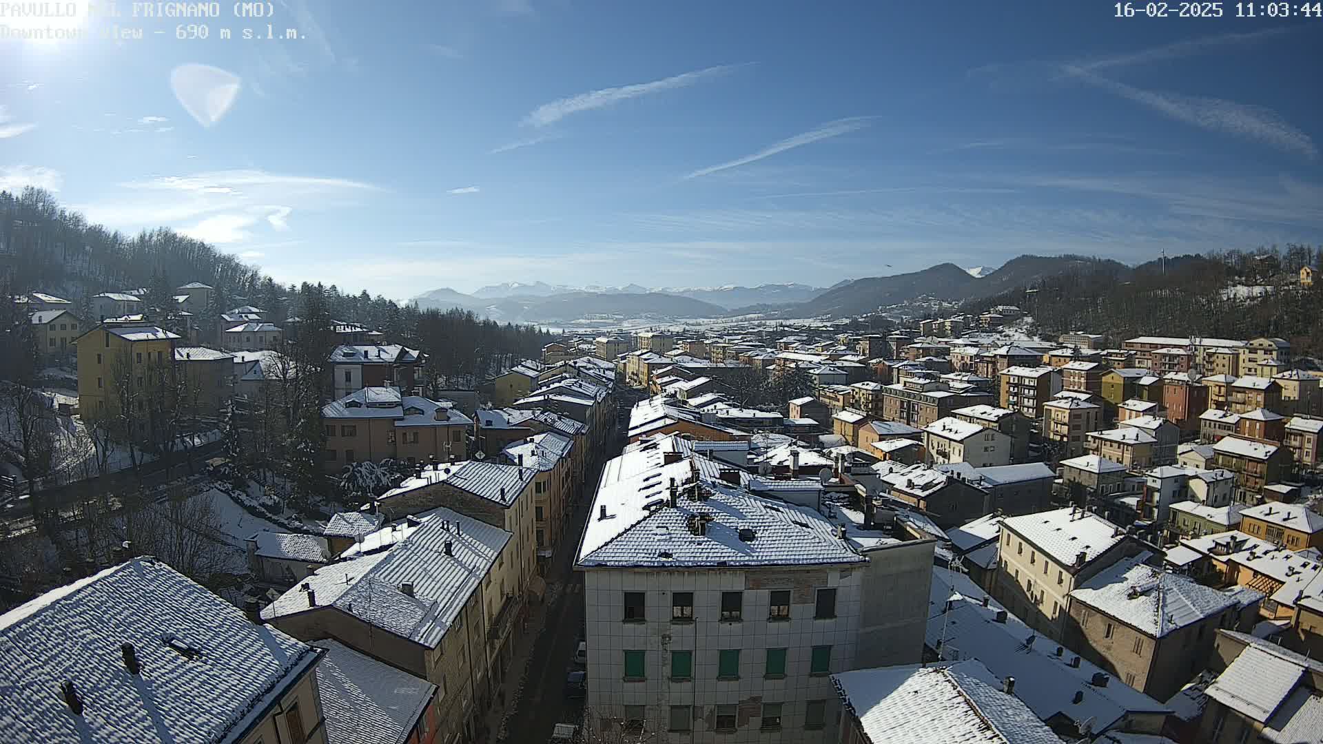 A snow-covered town nestled in a valley under a clear, sunny sky, with mountains visible in the distance.