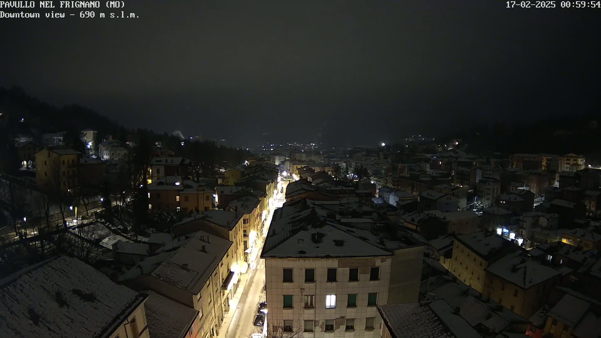 A nighttime aerial view of a snow-covered town under a dark, cloudy sky.