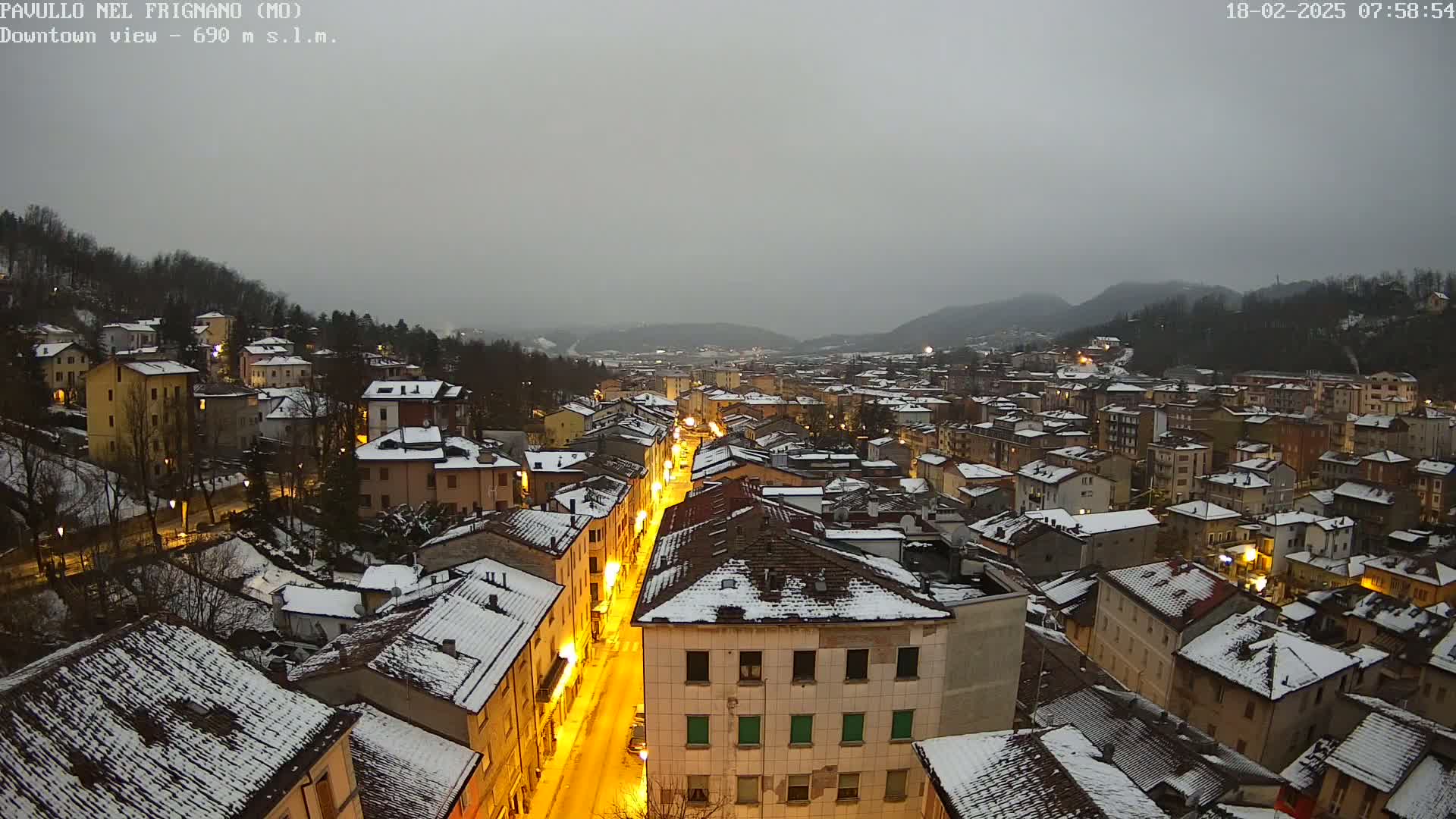 A snow-covered town at twilight, with illuminated streets winding through buildings nestled in a valley.