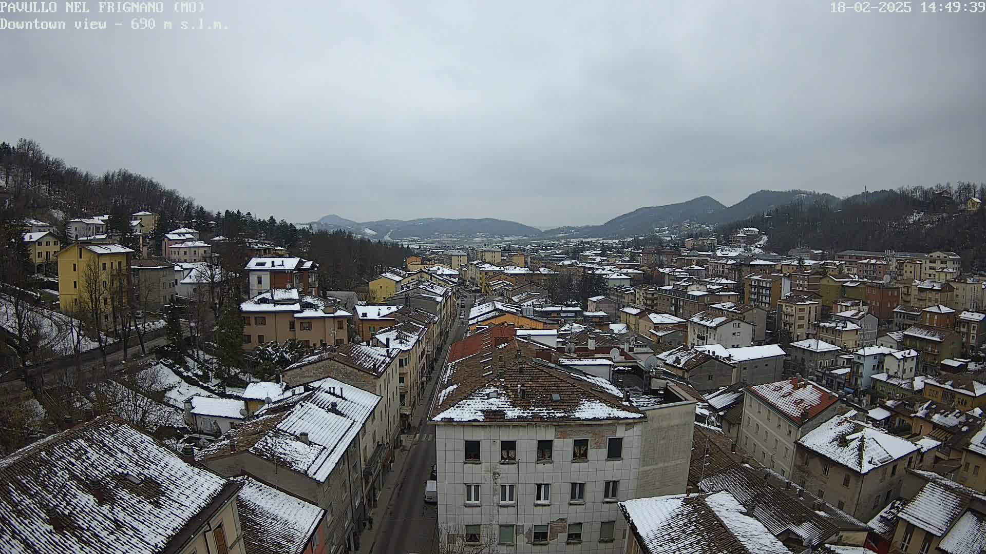 A snow-covered town nestled in a valley between hills under an overcast sky.