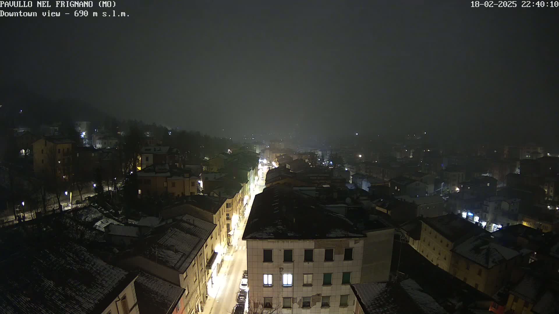 A nighttime, snowy scene overlooks a town's street and buildings, shrouded in fog.