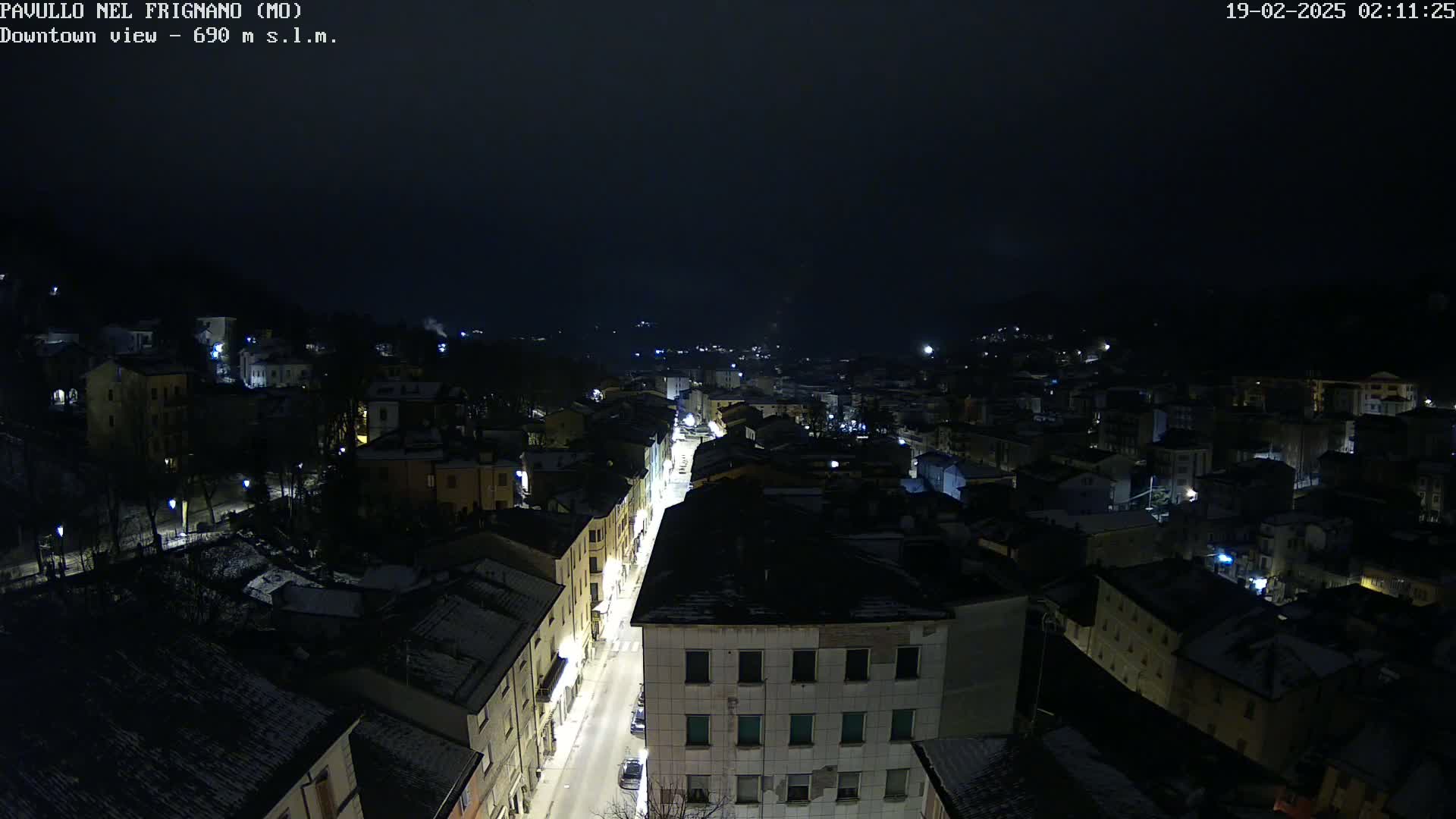 A nighttime, snow-dusted town is viewed from above, showing a main street illuminated with streetlights.