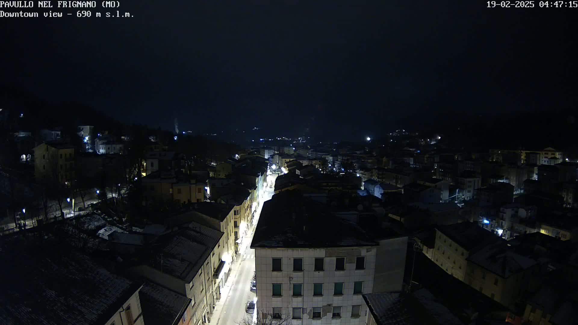 A nighttime, aerial view of a snow-dusted town with a brightly lit street running through its center under a dark sky.